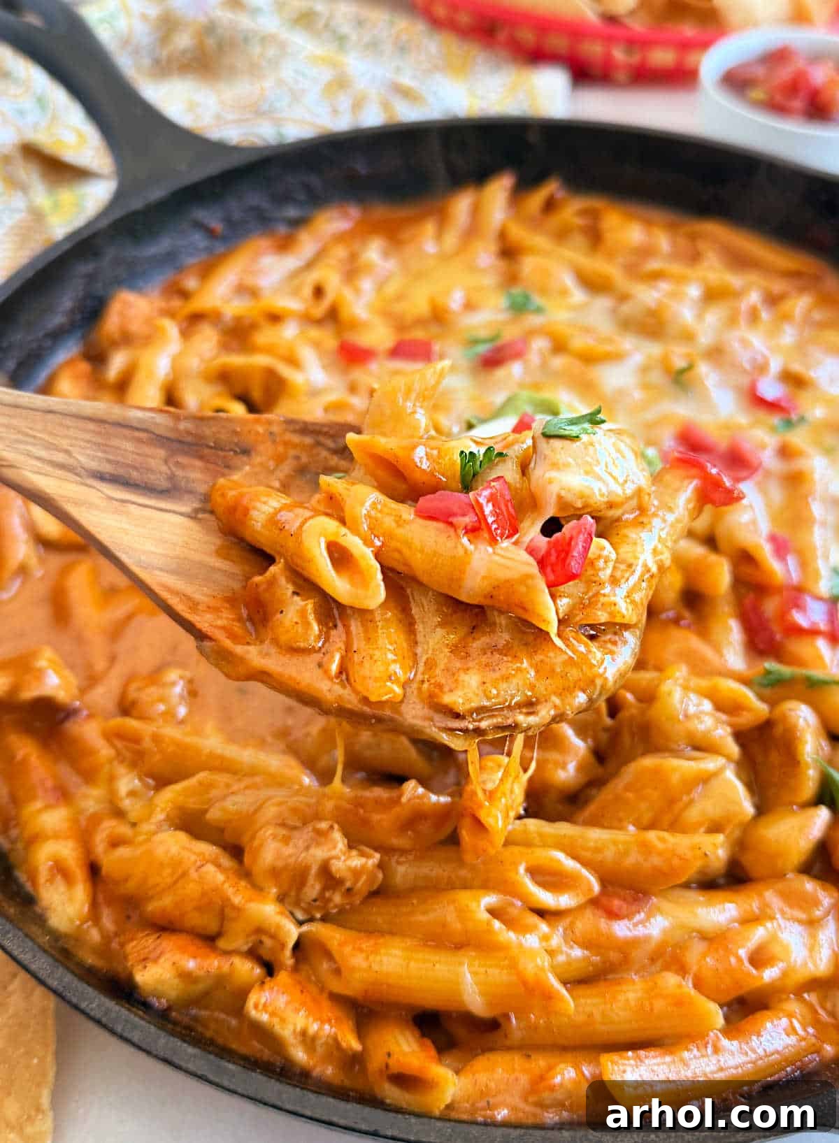 Close-up of creamy chicken enchilada pasta being served on a spoon from a skillet, highlighting the rich, cheesy sauce and tender chicken.