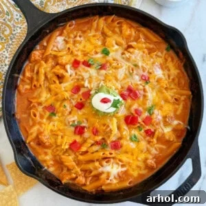 One-pan chicken enchilada pasta in a cast iron skillet, garnished with fresh cilantro and a dollop of sour cream.