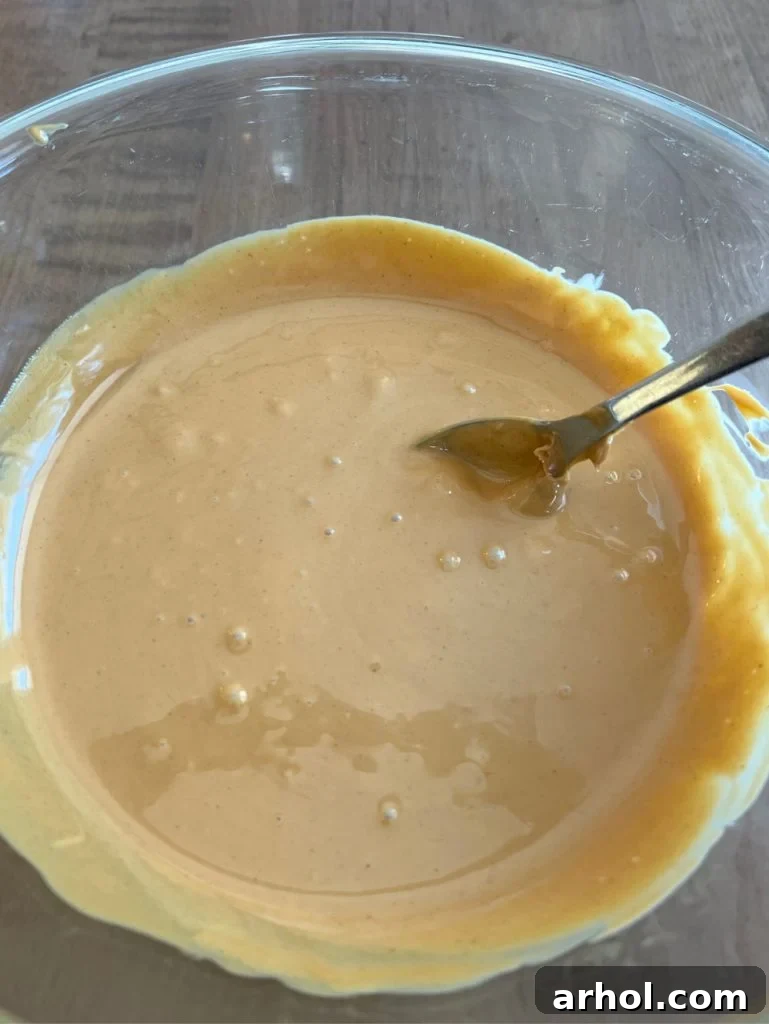 A close-up view of the rich, melted peanut butter and butterscotch chips, being stirred to a perfect, glossy consistency for the cookie base.