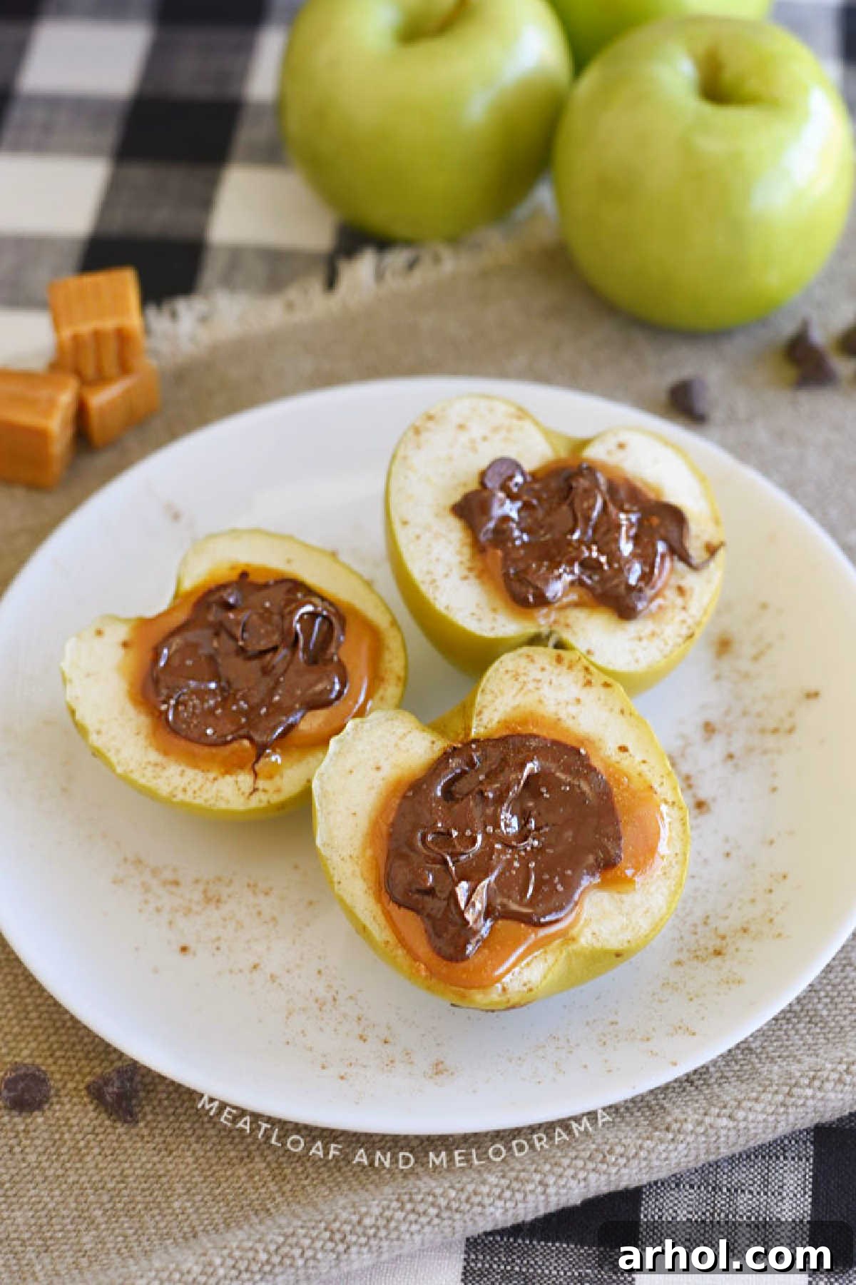Baked apples stuffed with caramel and melted chocolate on a plate, garnished with sea salt and cinnamon.