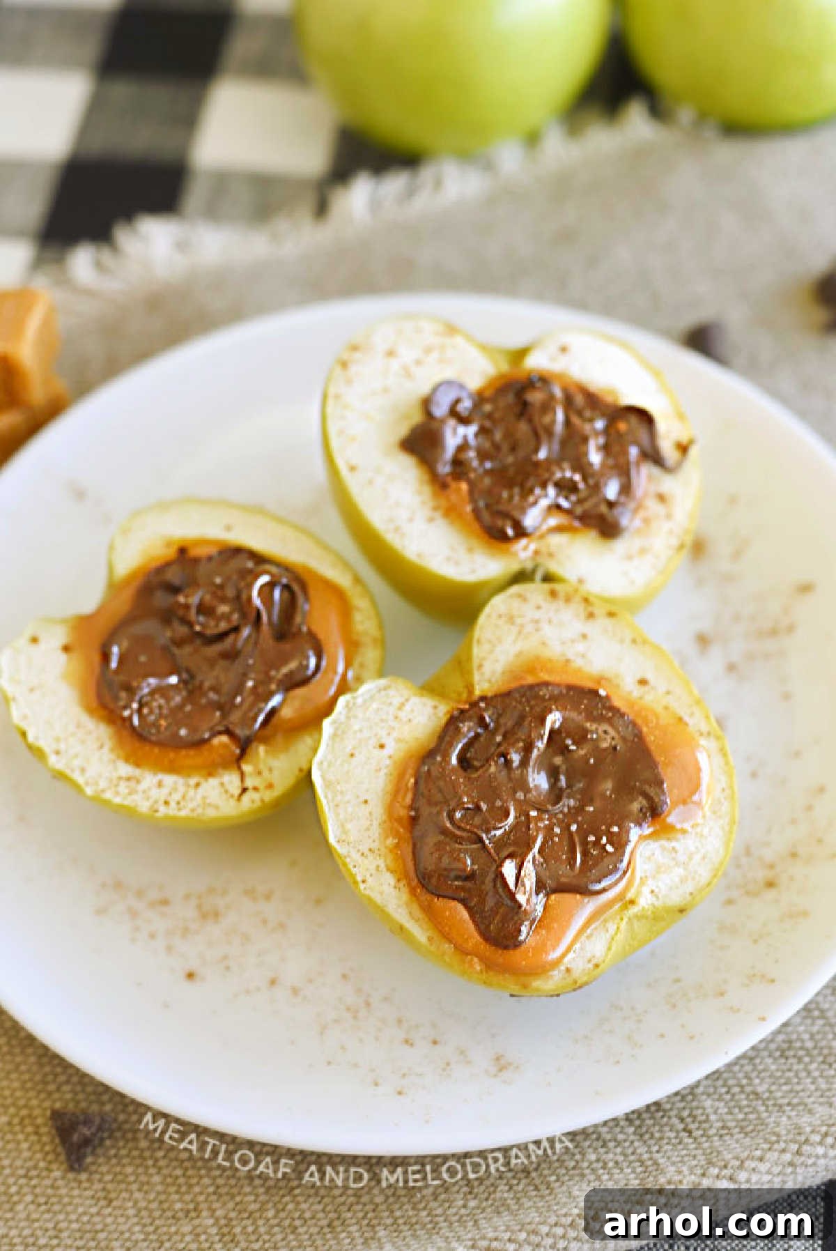 Two halves of baked apples with caramel in the middle and melted chocolate on top, ready for serving on a white plate.