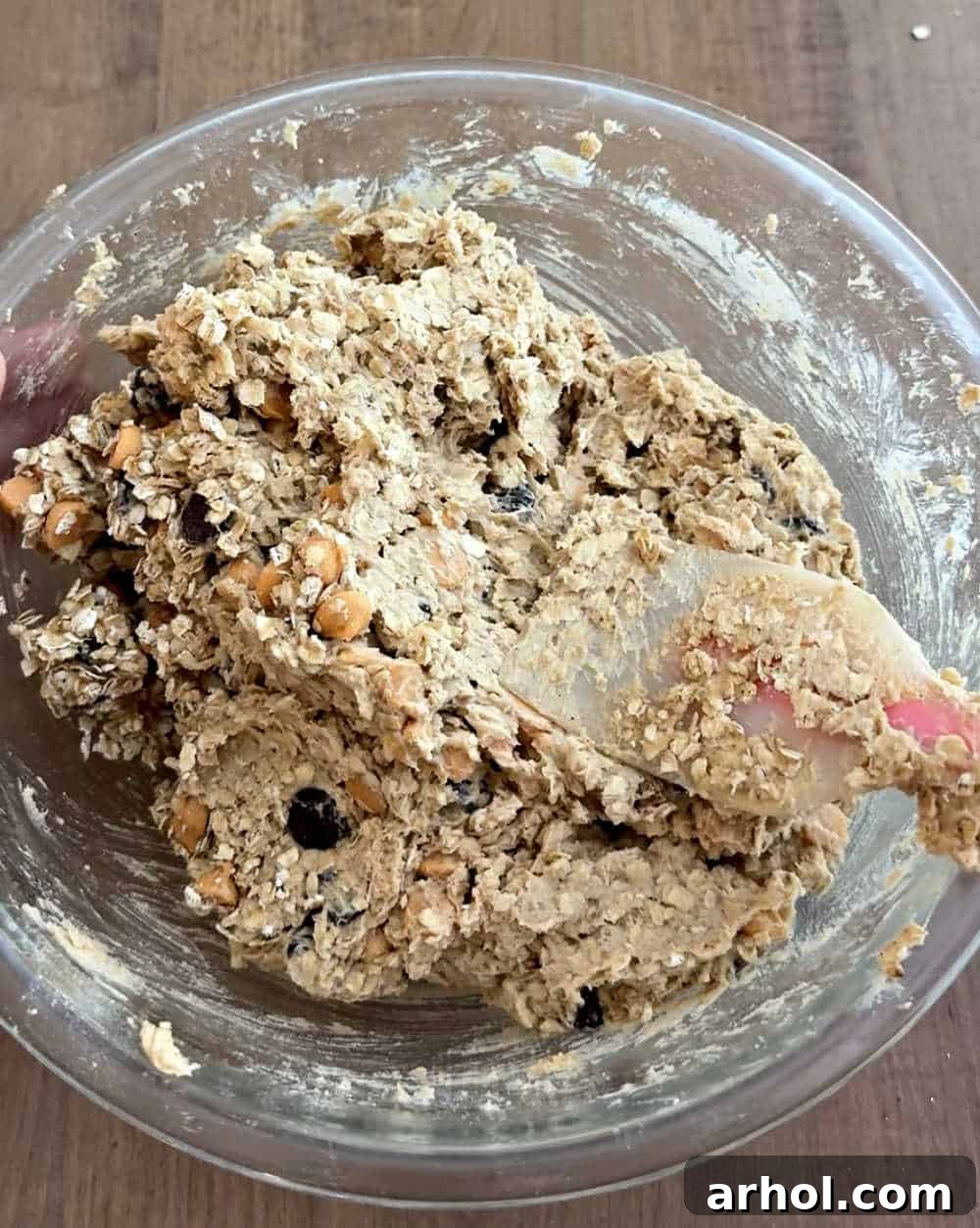 Folding in the old-fashioned oats, butterscotch chips, and chocolate chips into the cookie dough with a rubber spatula.