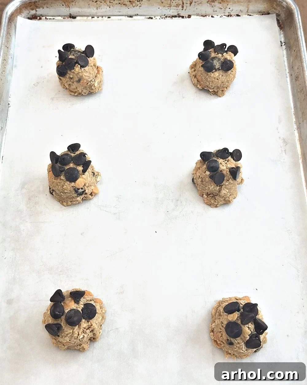 Scooped cookie dough balls, topped with extra chocolate chips, resting on a parchment-lined baking sheet before chilling.