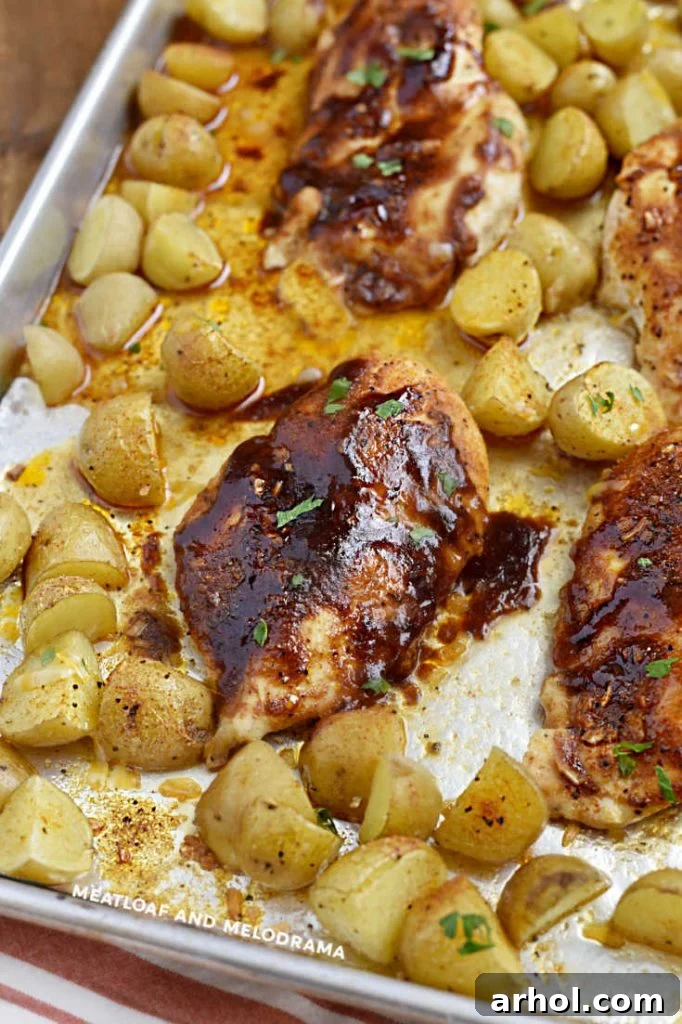 baked chicken breasts with bbq sauce and baby potatoes on a baking sheet