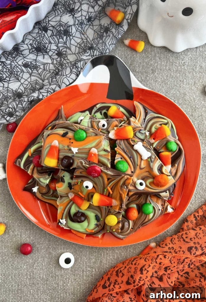 Festive Halloween candy bark adorned with candy corn and various Halloween candies, artfully arranged on a pumpkin-themed serving plate.