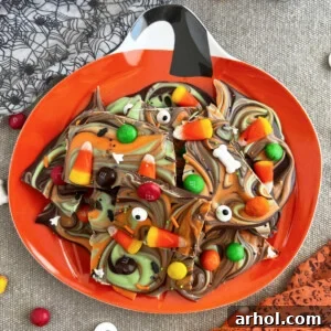 A delightful piece of Halloween candy bark, featuring candy corn and other festive Halloween candies, resting on a charming jack-o'-lantern themed plate.
