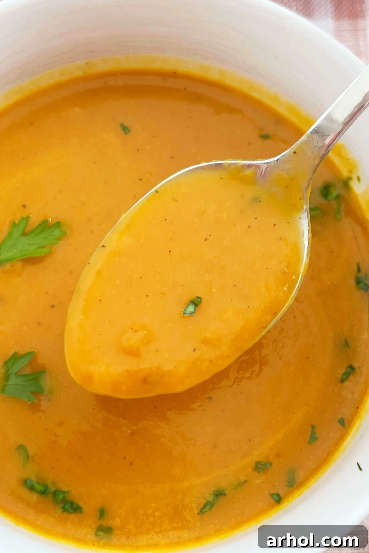 A spoonful of creamy savory pumpkin soup made with canned pumpkin, held over a rustic white bowl, garnished with fresh parsley.