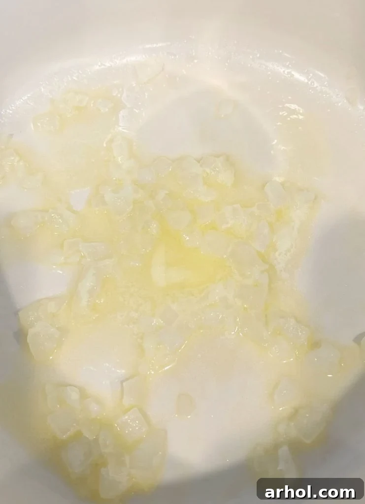 Finely chopped white onions are being sautéed in melted butter within a red Dutch oven, becoming soft and translucent.