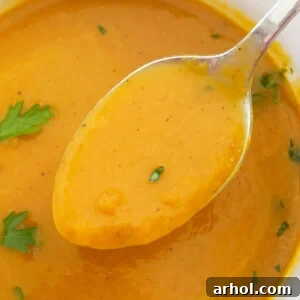 A close-up of creamy pumpkin soup made with canned pumpkin on a spoon, garnished with fresh parsley, held over a white bowl.