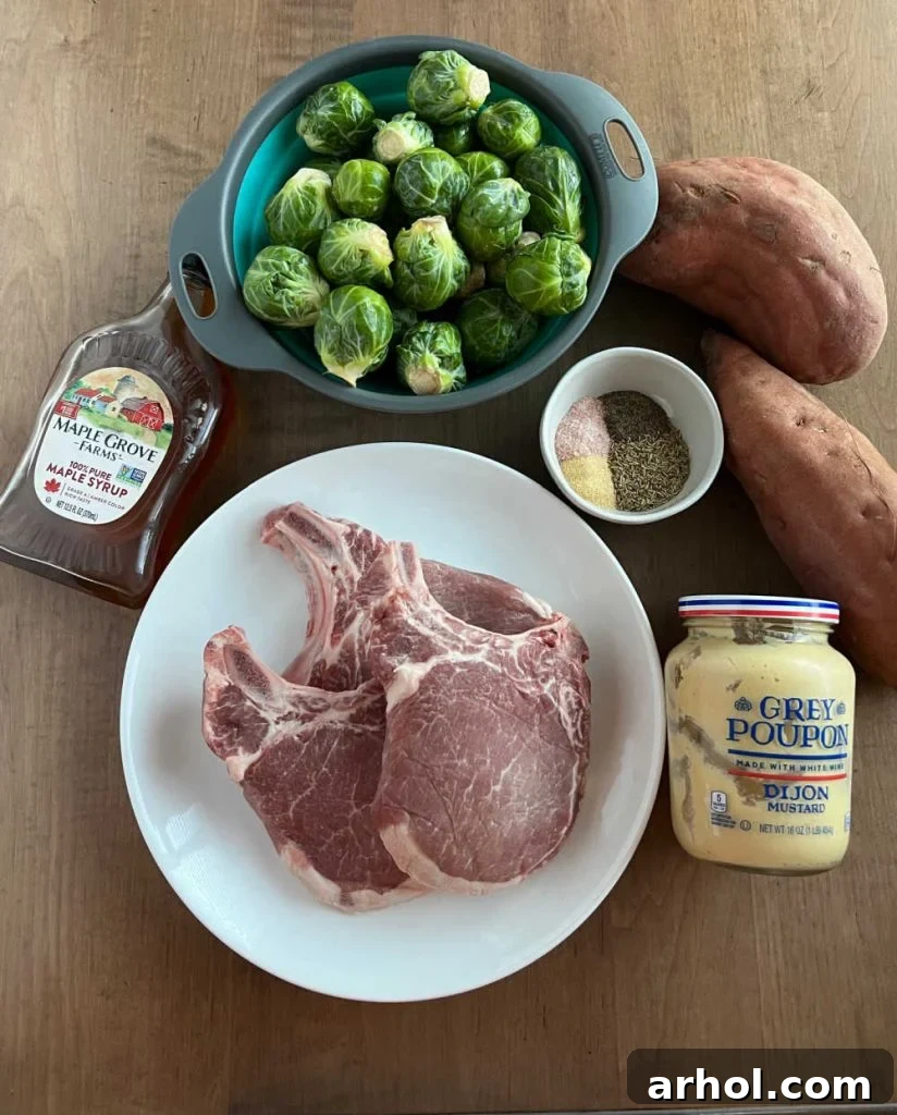 Bone-in pork chops, Brussels sprouts, sweet potatoes, maple syrup, mustard and seasonings laid out for cooking.