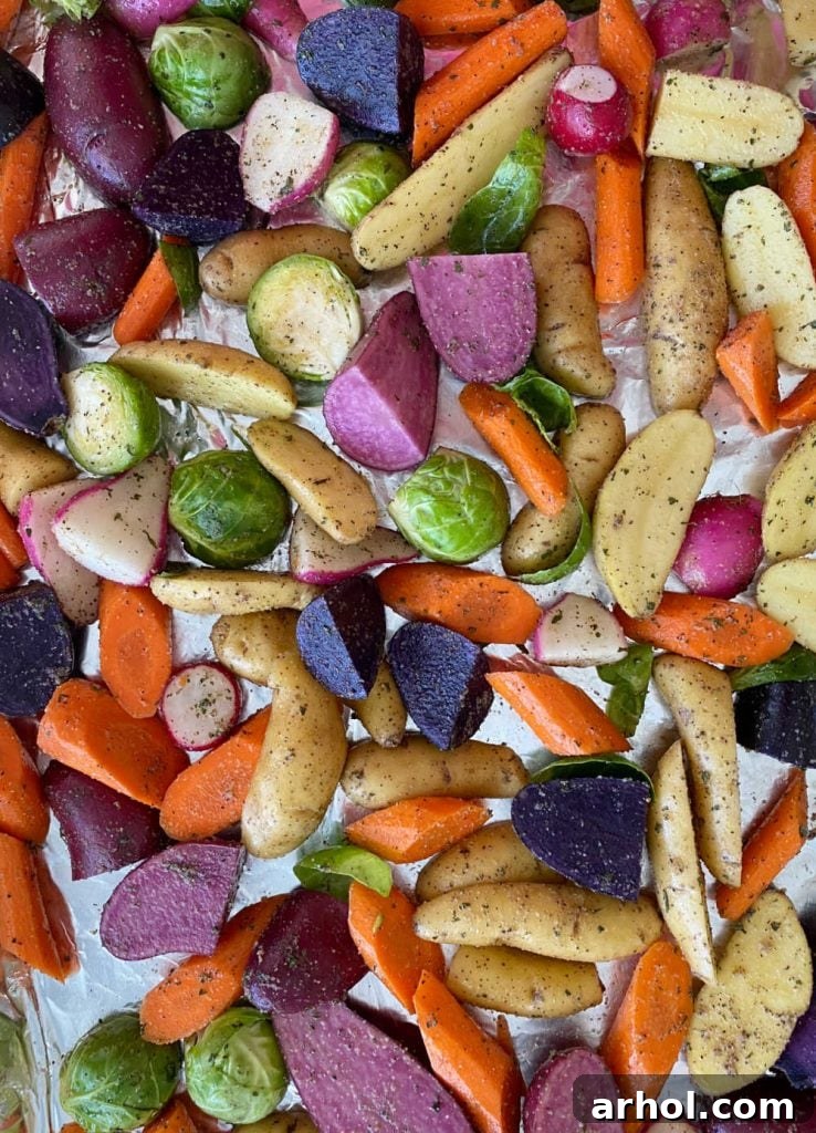 Raw, seasoned root vegetables and Brussels sprouts spread in a single layer on a parchment-lined baking sheet, ready for the oven.