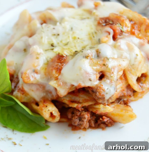 A large rectangular baking dish overflowing with Cheesy Baked Penne Pasta, fresh out of the oven, with melted cheese and rich sauce visible.