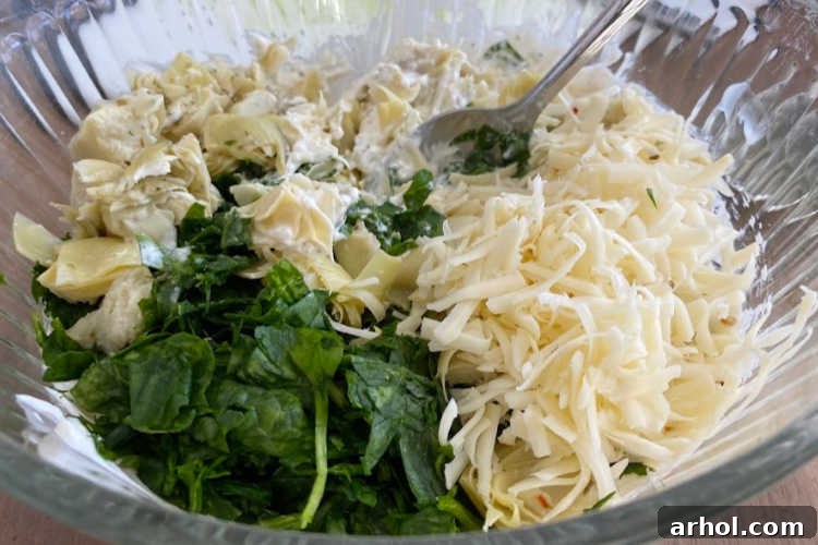 Ultimate Creamy Baked Spinach Artichoke Dip 4 Adding fresh spinach, chopped artichoke hearts, and pepper jack cheese to the creamy mixture in a bowl.