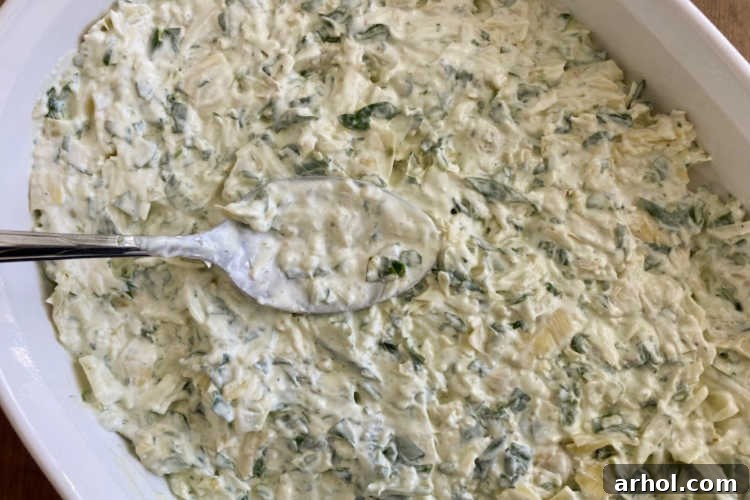 Ultimate Creamy Baked Spinach Artichoke Dip 5 Spreading the creamy spinach artichoke dip mixture into a casserole dish before baking.