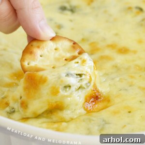 Ultimate Creamy Baked Spinach Artichoke Dip 7 Round cracker dipped into hot, cheesy spinach artichoke dip, emphasizing its creamy texture.