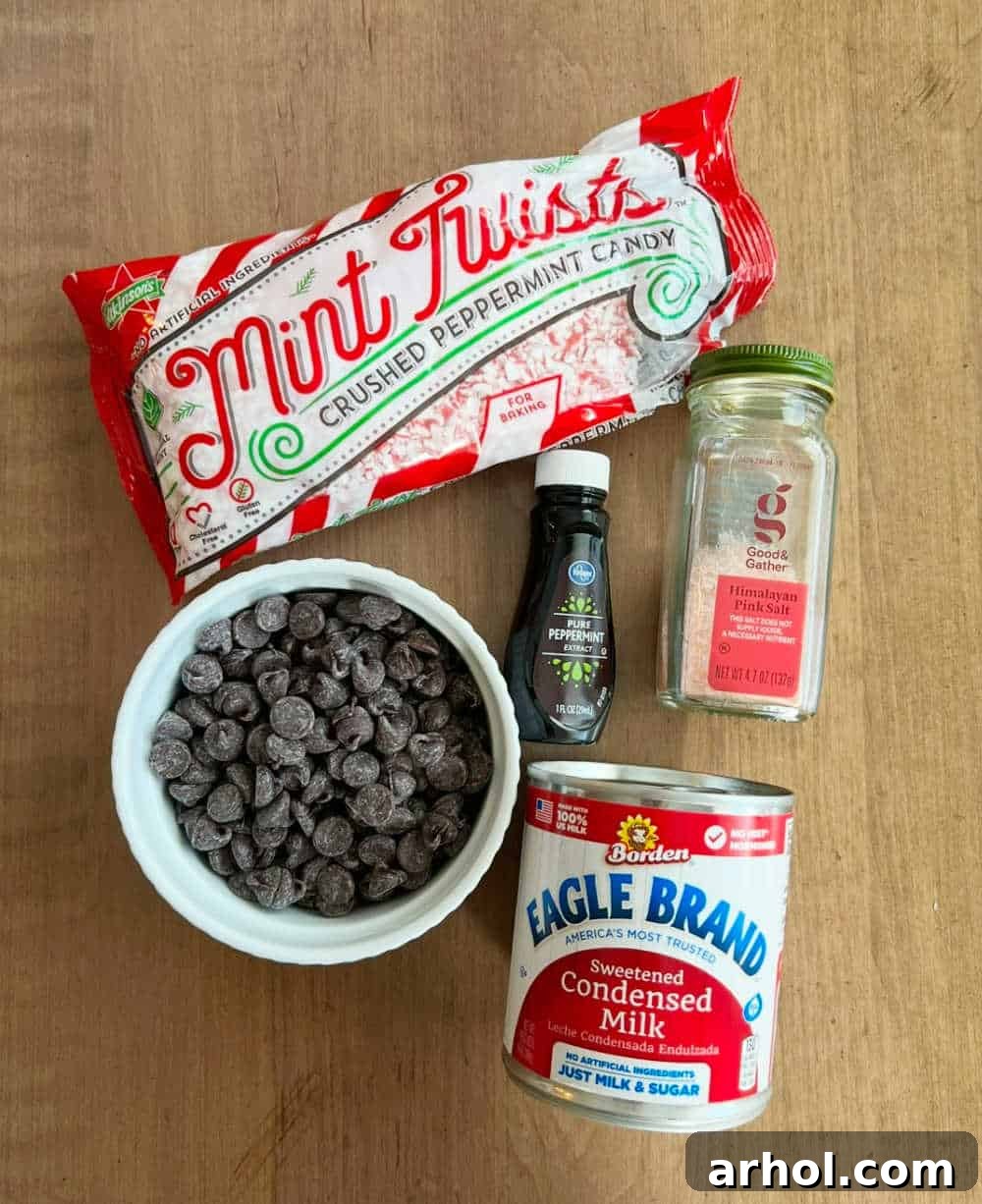 Sweetened condensed milk, semi-sweet chocolate chips, sea salt, peppermint extract, and crushed peppermint candies, laid out on a surface.