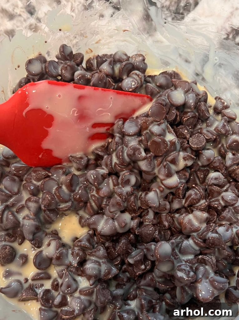 Melting chocolate chips and sweetened condensed milk in a microwave-safe bowl, being stirred for smooth consistency.