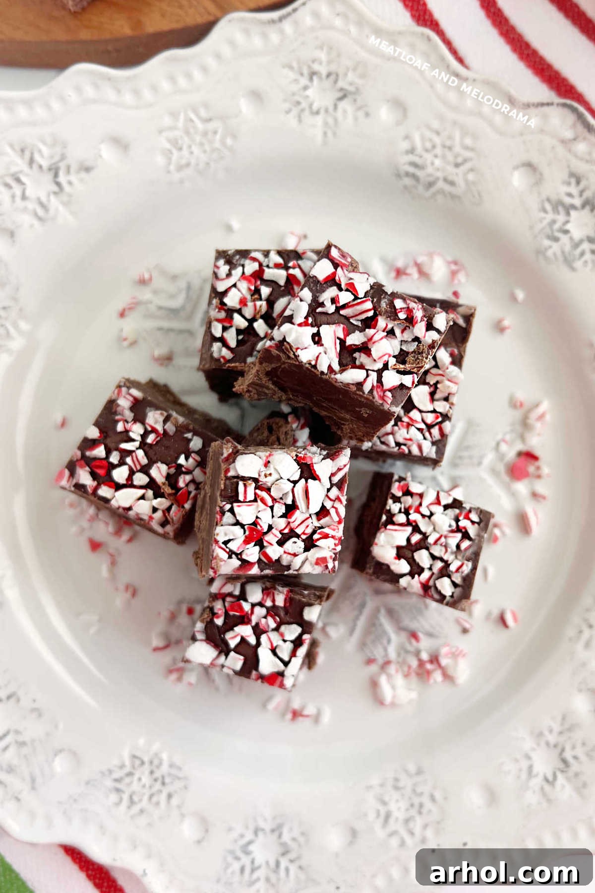 Rich, dark chocolate peppermint fudge cut into squares with crushed peppermint candy on top, arranged enticingly on a white plate.