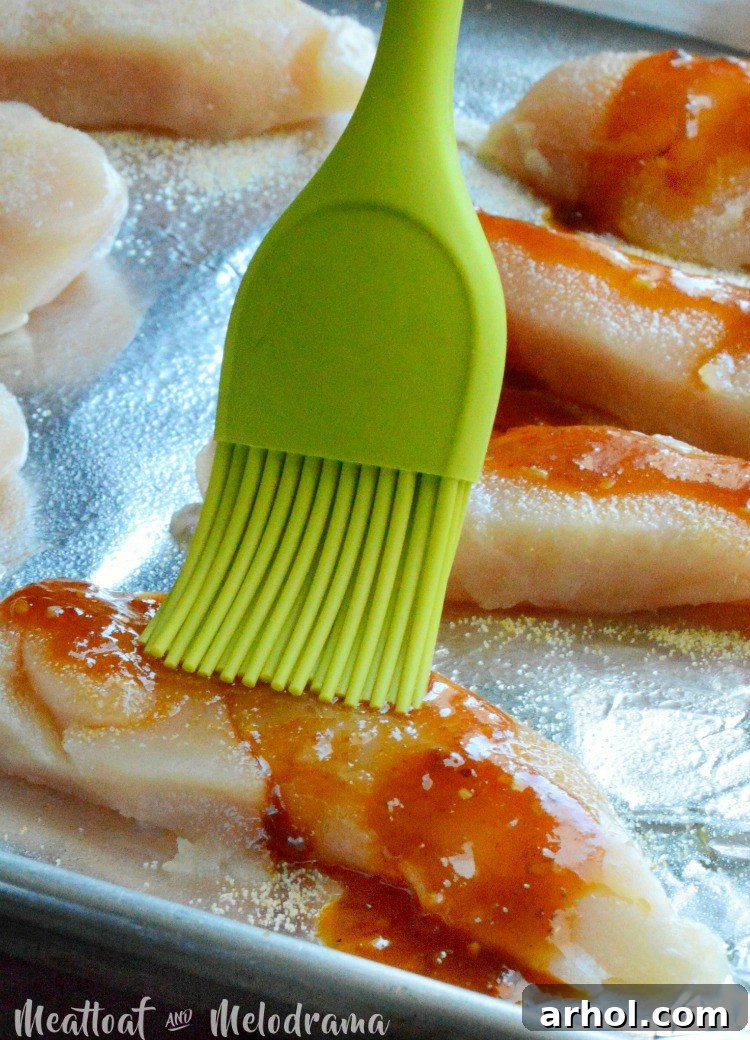 Brushing honey chipotle sauce onto raw chicken tenders on a baking sheet
