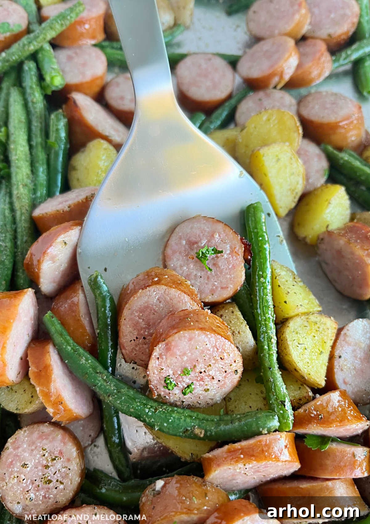 Smoked sausage and potatoes with fresh green beans on a metal spatula, ready to serve from the sheet pan.