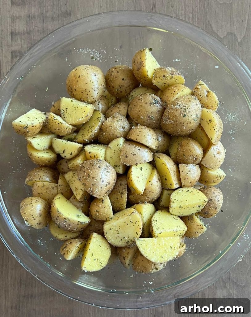 Cut baby potatoes tossed with olive oil and spices in a clear glass bowl, ready for roasting.