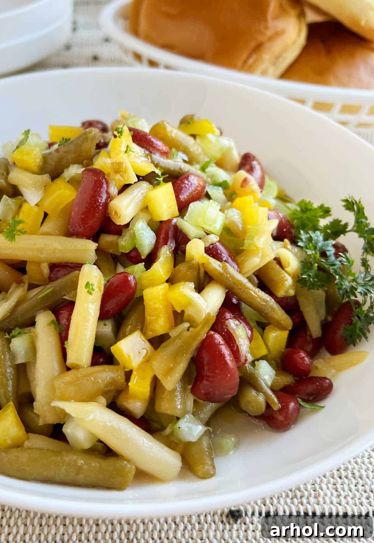 Grandma's classic three bean salad served in an elegant glass bowl, garnished with fresh herbs, ready for sharing at a summer gathering.