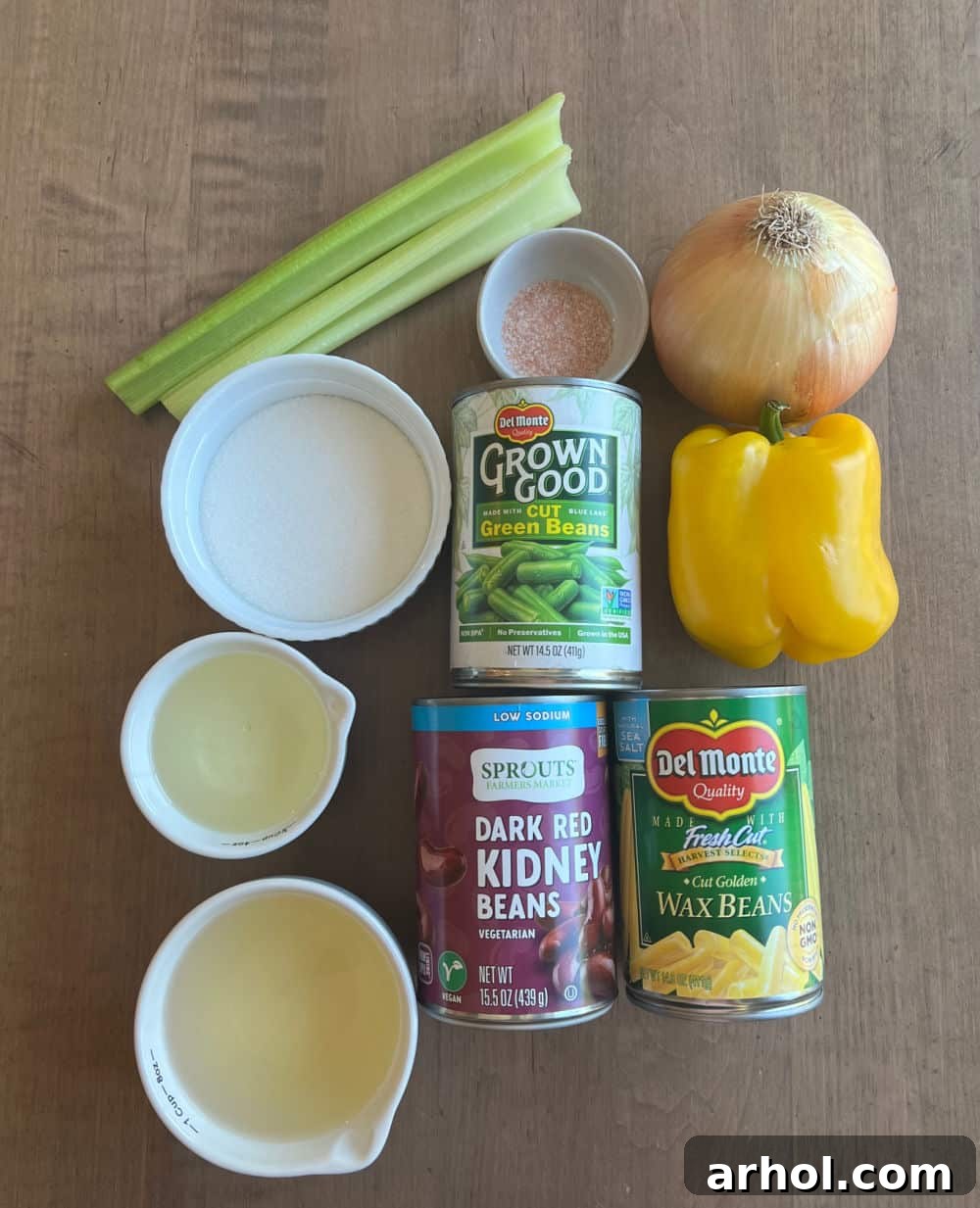 A vibrant selection of fresh ingredients laid out for making three bean salad, including canned green beans, wax beans, kidney beans, crisp celery, colorful bell peppers, and a red onion, all ready for preparation.