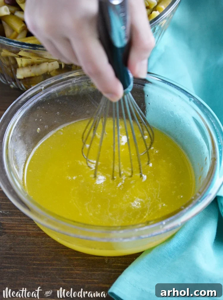 A simple, tangy salad dressing being expertly whisked vigorously in a clear glass bowl, creating a perfect emulsion, ready to be poured over the bean mixture.