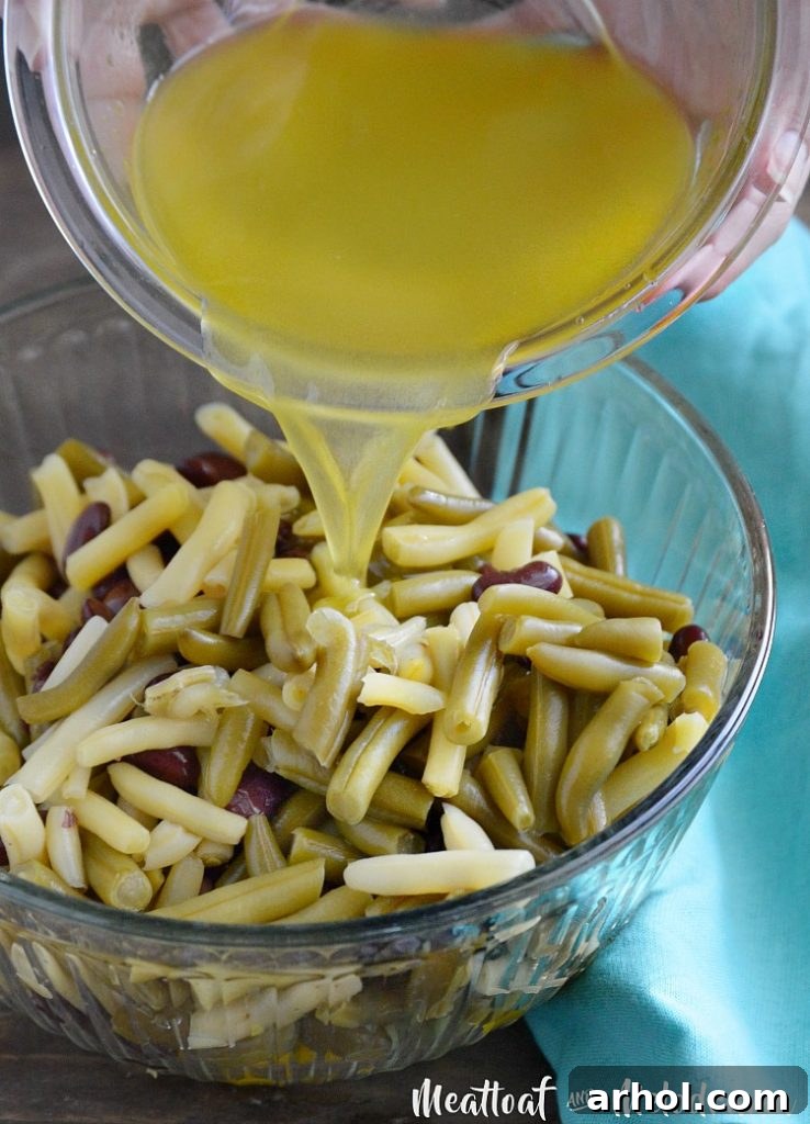 The vibrant, freshly whisked dressing being carefully poured over a large bowl brimming with an assortment of colorful beans and finely chopped fresh vegetables, poised for thorough mixing.