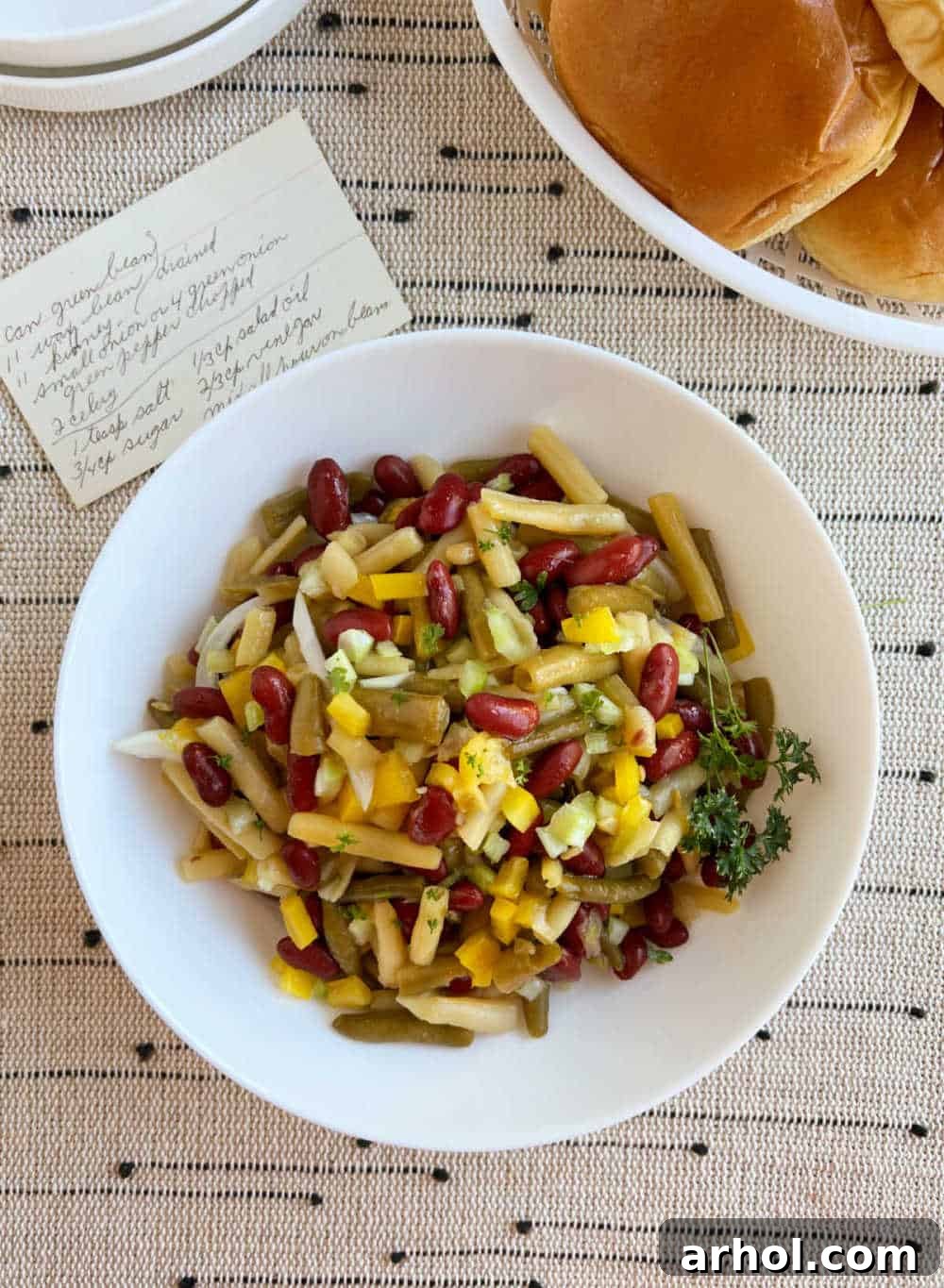 A rustic presentation of three bean salad in a serving bowl, elegantly accompanied by a handwritten family recipe card, beautifully emphasizing its cherished traditional heritage and homemade charm.