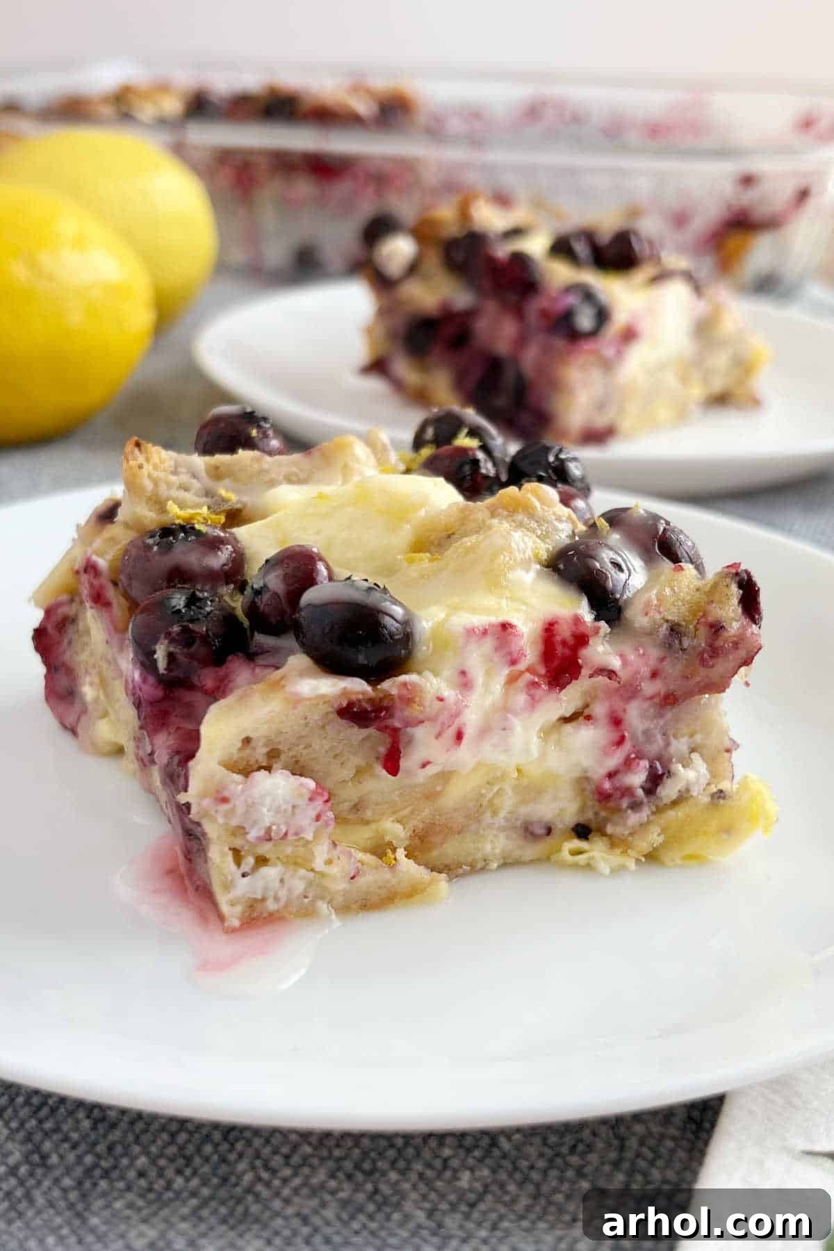 A delectable slice of Lemon Blueberry Bagel Breakfast Casserole, showcasing golden-baked bagels, melted cream cheese, and juicy blueberries, served on a white plate.