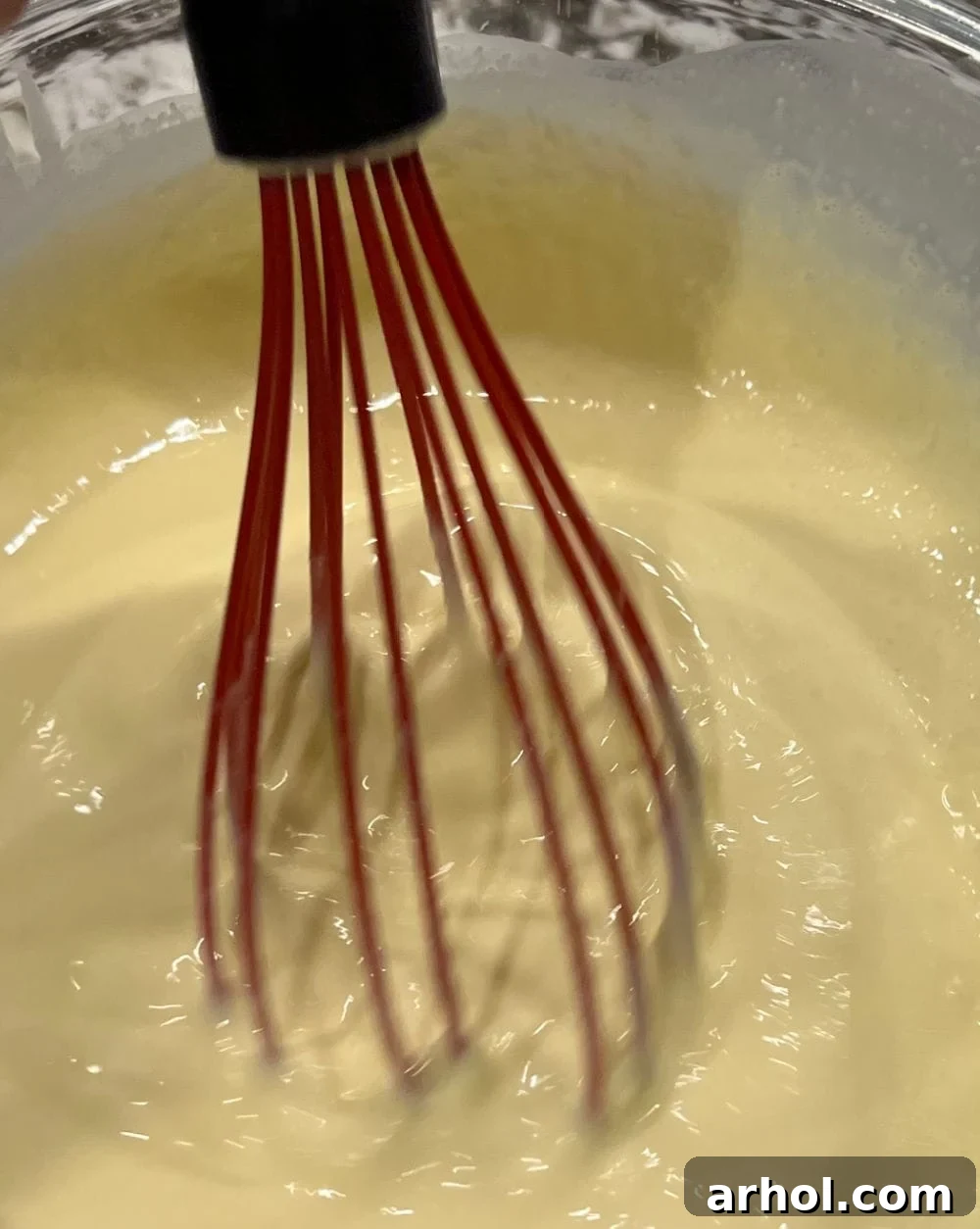 Hands whisking eggs and heavy cream in a bowl, preparing the custard for the casserole.