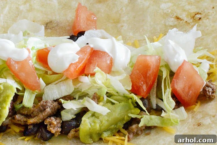 ground beef with lettuce, tomatoes, cheese and sour cream in a tortilla