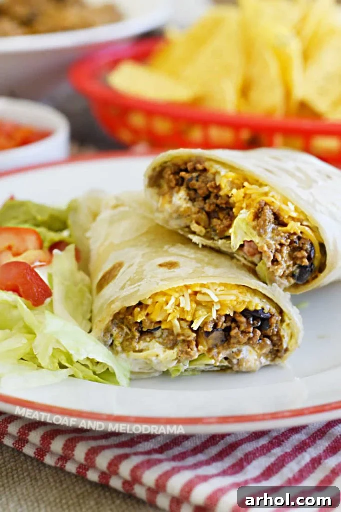 cut open ground beef burritos on a plate with lettuce and tomatoes