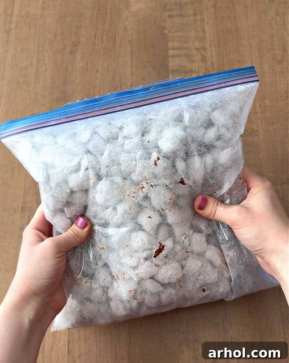 A clear freezer bag is being shaken to coat puppy chow with powdered sugar.