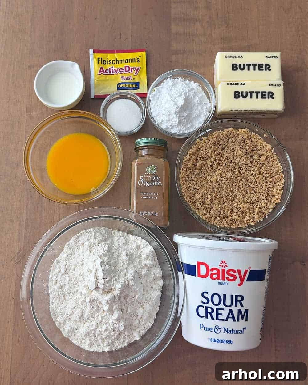 A carefully arranged flat lay of essential ingredients for making nut horns, including butter, flour, yeast, sugar, cinnamon, milk, sour cream, walnuts, and eggs.