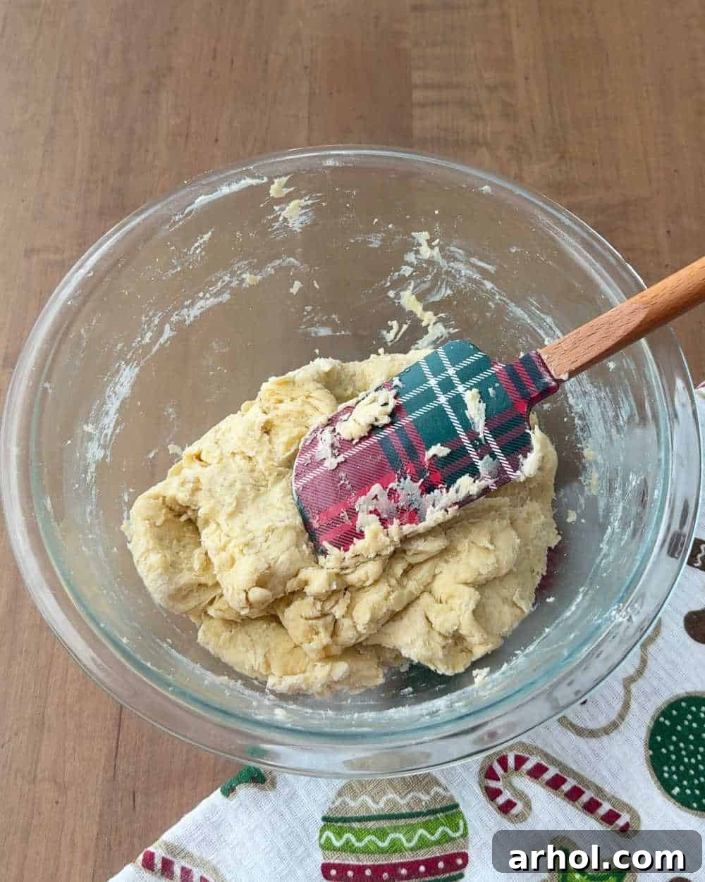 Incorporating flour into the dough using a plaid spatula, showing a soft, forming dough.
