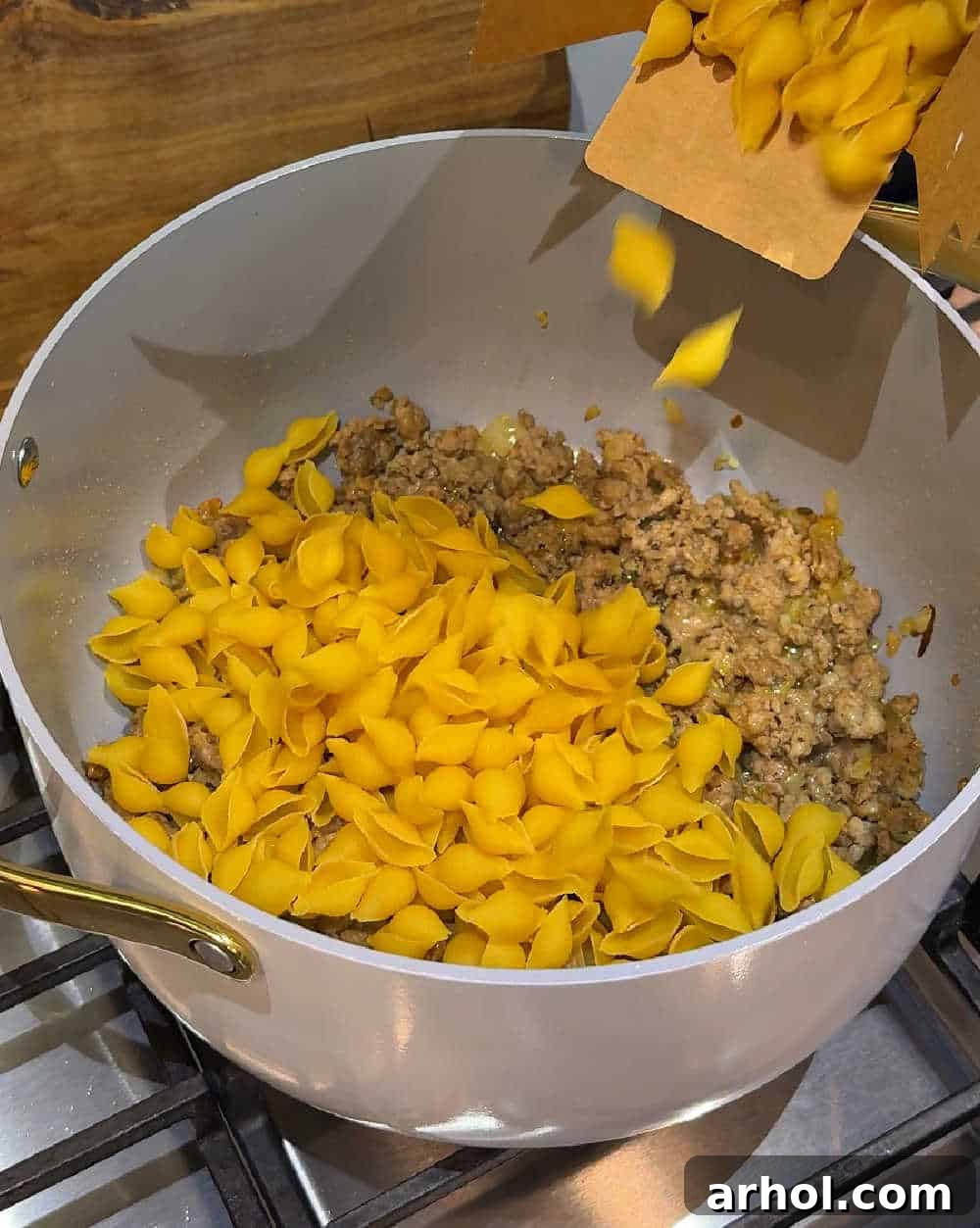 Step 2: Adding uncooked pasta shells to the pot with browned sausage.