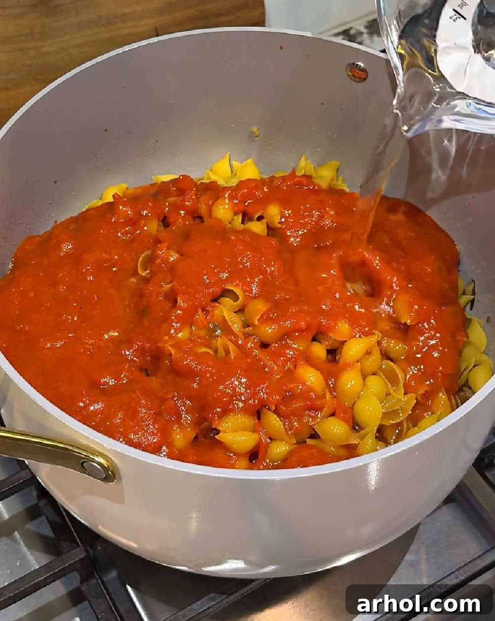 Step 3: Pouring marinara sauce and water over the pasta and sausage.