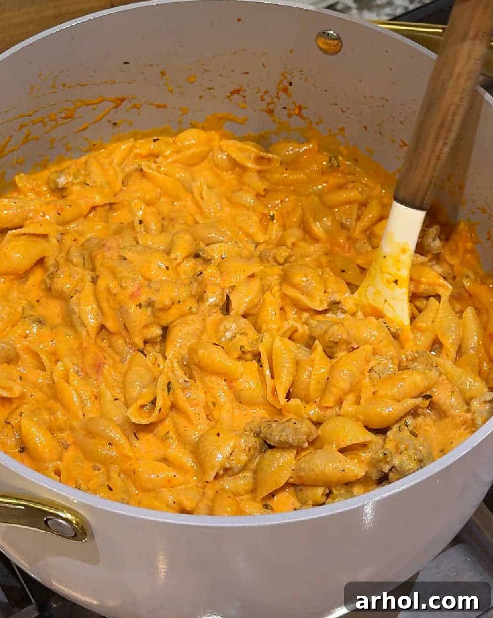 Step 4: Stirring the creamy sausage and shells pasta in the pot with a wooden spoon.