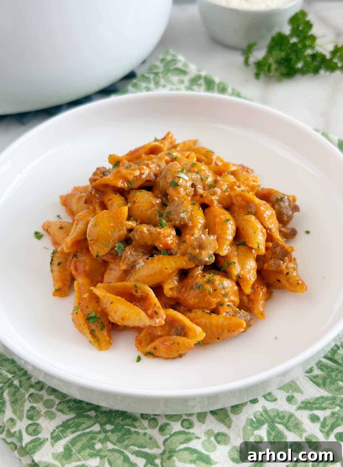 A serving of creamy sausage pasta on a white plate, garnished with fresh parsley.