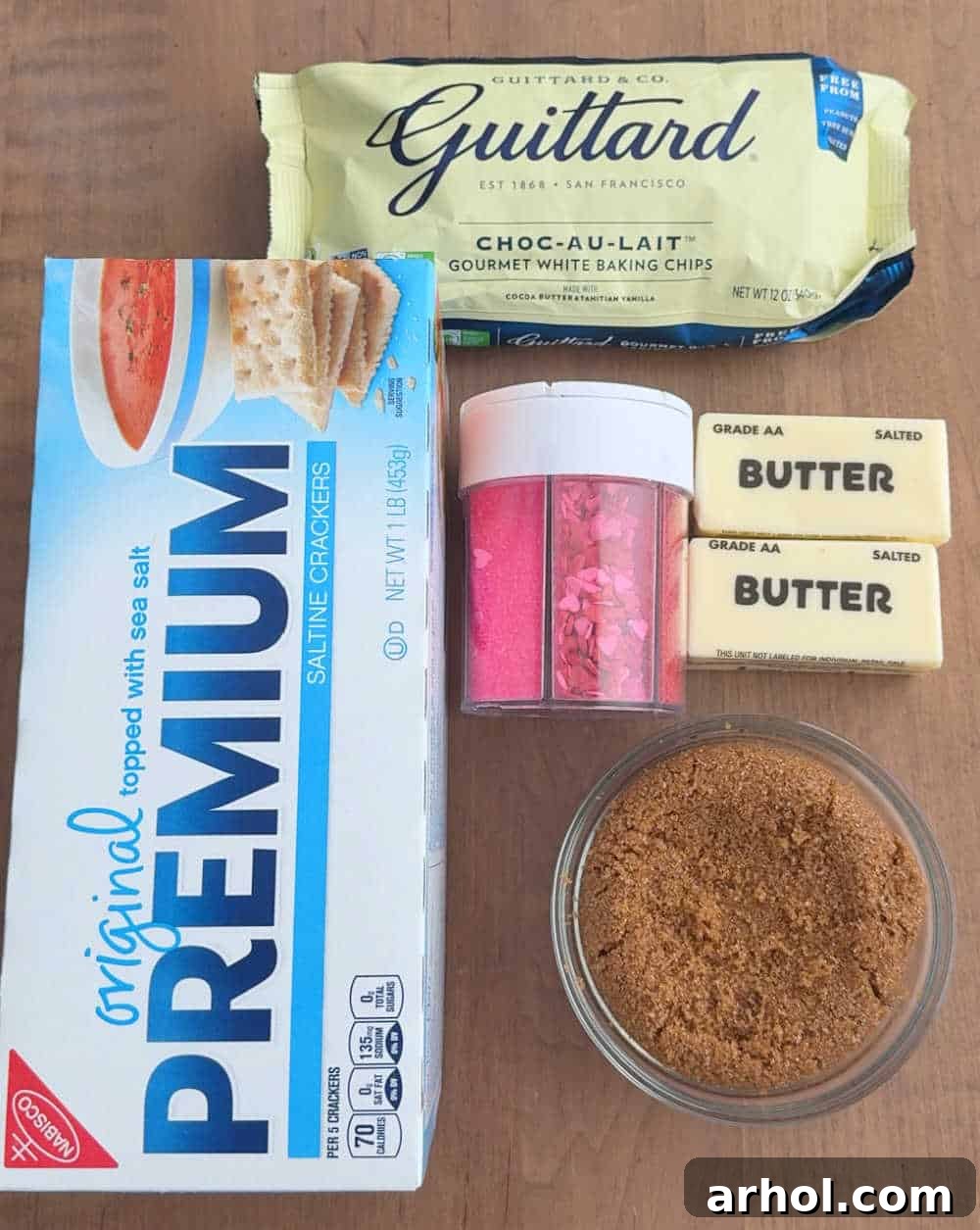 Arrangement of essential ingredients: saltine crackers, white chocolate chips, butter, brown sugar, and a bowl of colorful sprinkles.