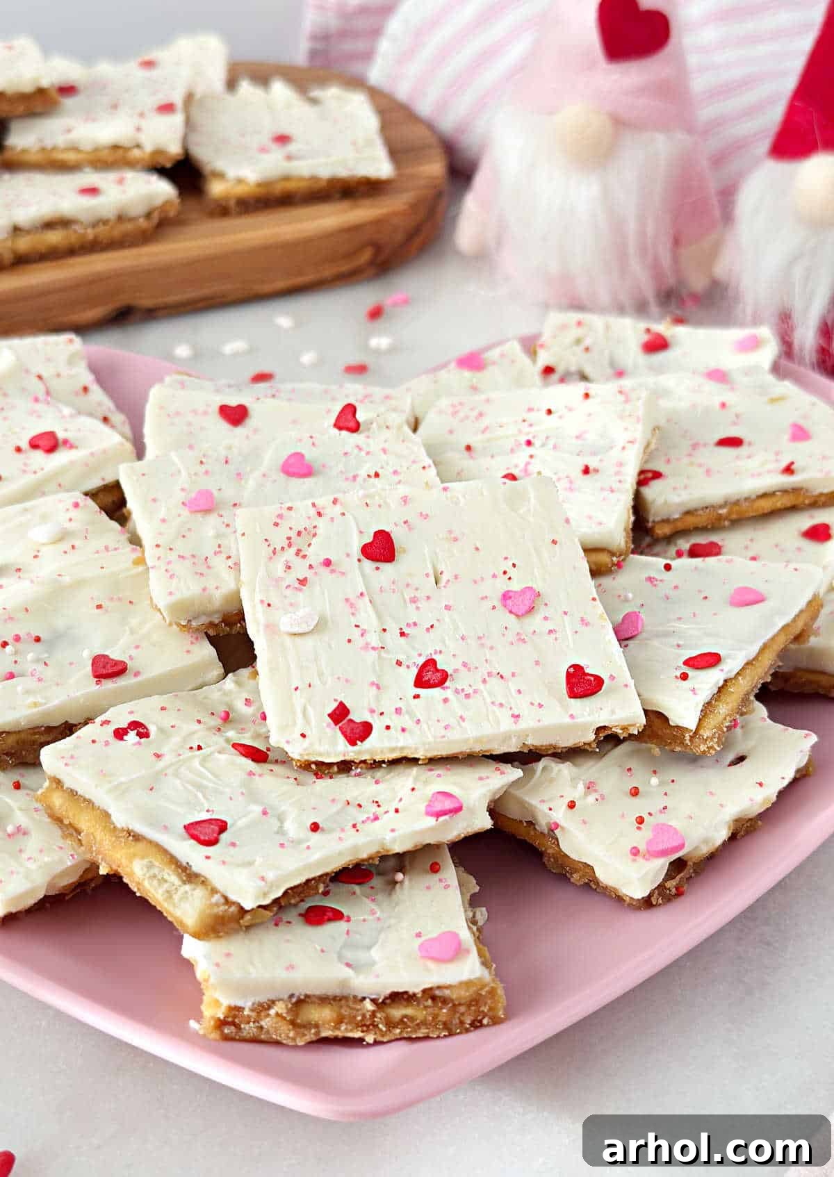 A stunning close-up of Valentine's Day Saltine Cracker Toffee, showing the crisp cracker base, rich caramel, and white chocolate top with sprinkles, artfully arranged on a decorative plate.