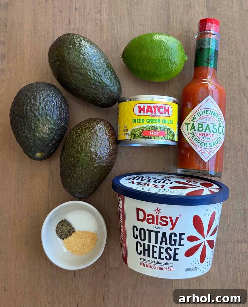 Avocados, canned green chiles, hot sauce, lime, cottage cheese, and various spices laid out on a wooden board, ready for the dip preparation.