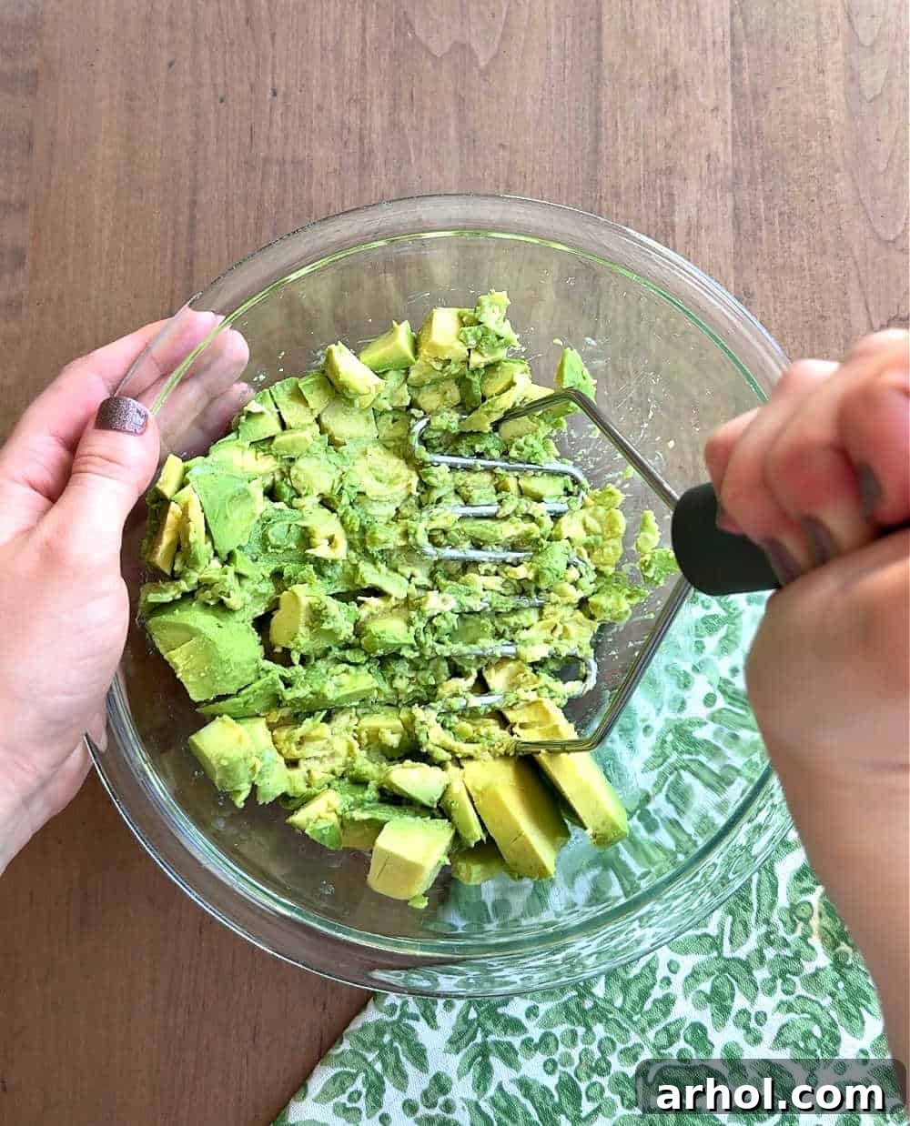 Mashing avocado in a mixing bowl with a fork, showing its creamy texture.