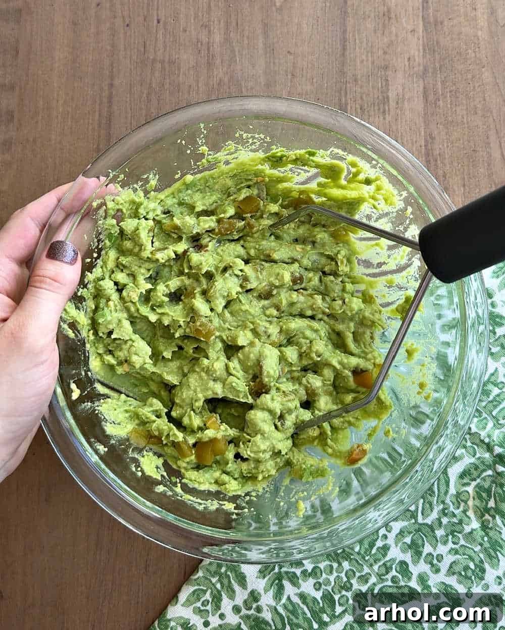 Incorporating green chiles into the mashed avocado mixture in a mixing bowl.