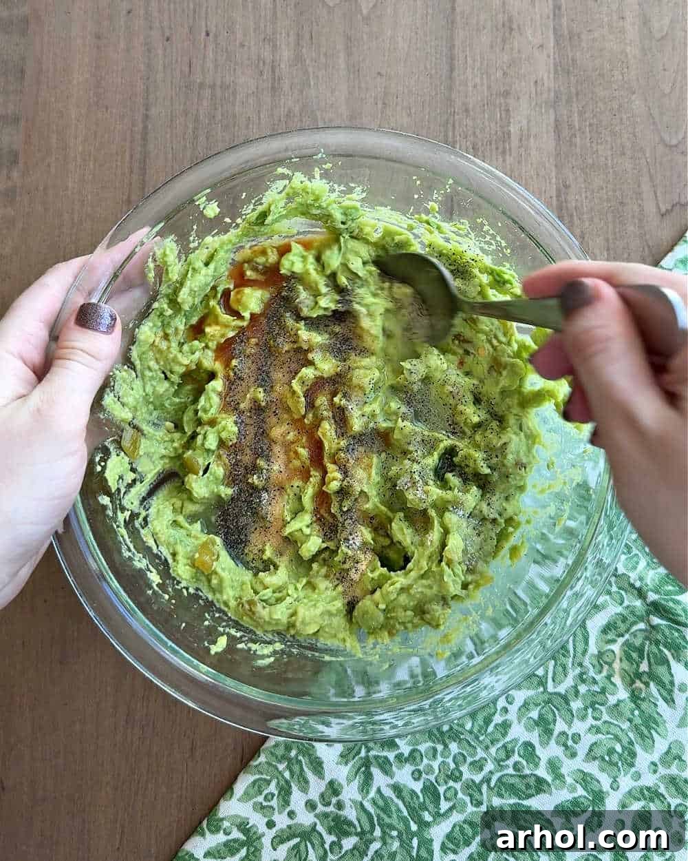 Mixing various spices like salt, pepper, and garlic powder into the avocado dip.
