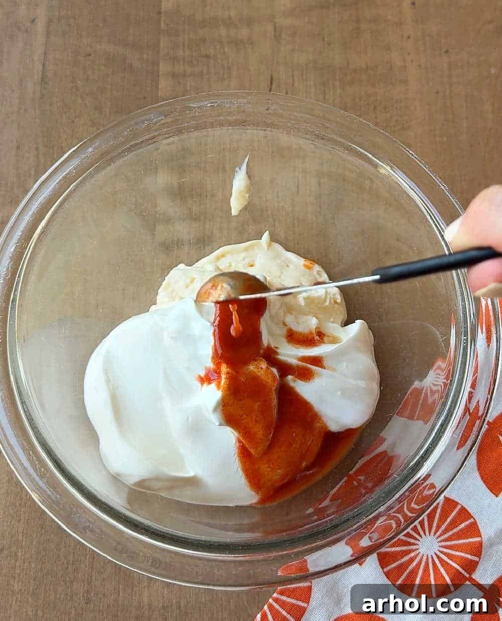 Adding ghost pepper puree to a bowl of mayonnaise and sour cream base, ready to be mixed for the spicy dip.