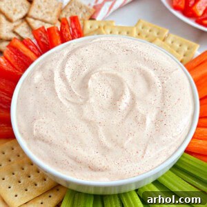 A bowl of ghost pepper dip prominently displayed with various dippers like fresh vegetables and crackers arranged around it.