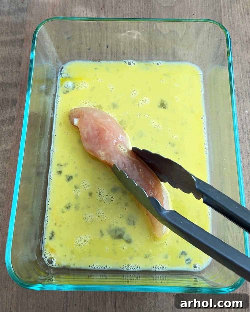 Dipping raw chicken tender into a bowl of egg wash.